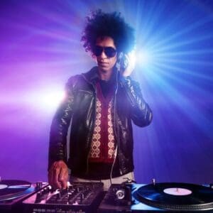 A man in leather jacket and sunglasses standing at the dj booth.